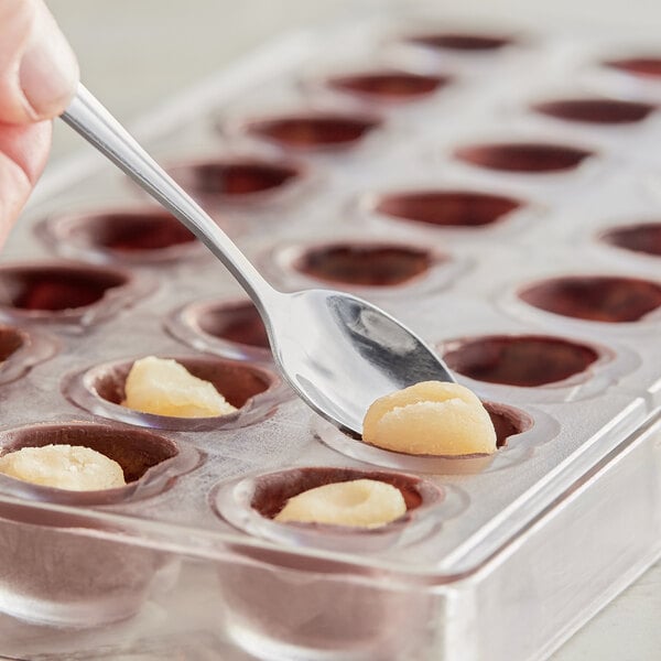 A spoon in a plastic tray with small round holes filled with chocolate.