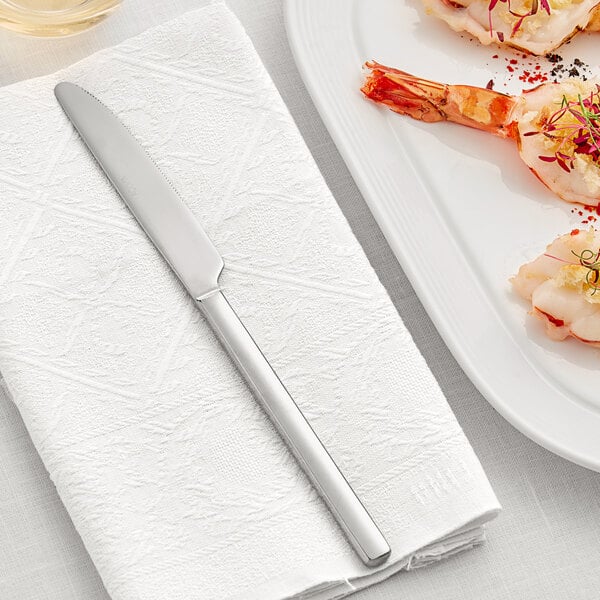 An Acopa stainless steel dinner knife on a white plate with shrimp.