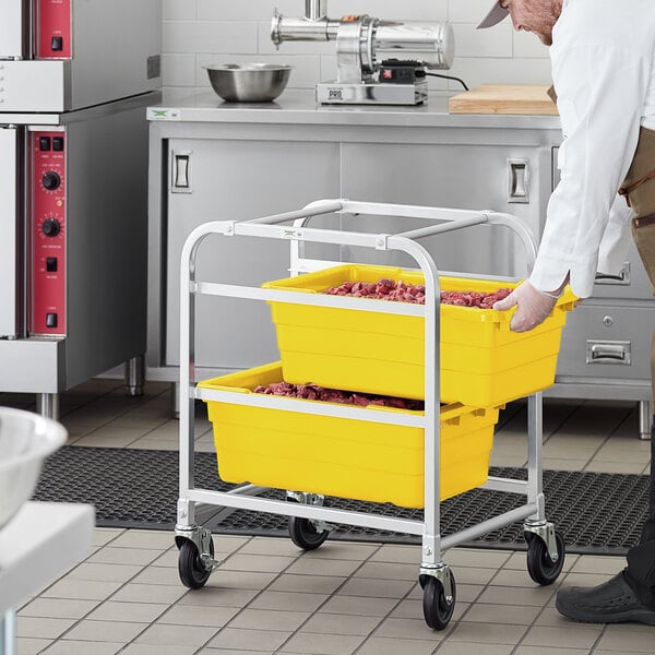 A man using a Regency aluminum lug rack to move yellow tote boxes full of food.