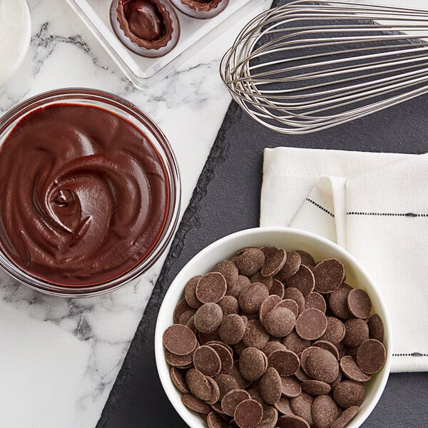A bowl of Cacao Barry dark chocolate pistoles with a whisk.