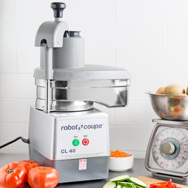 A Robot Coupe CL40 continuous feed food processor filled with shredded carrots on a counter in a professional kitchen.