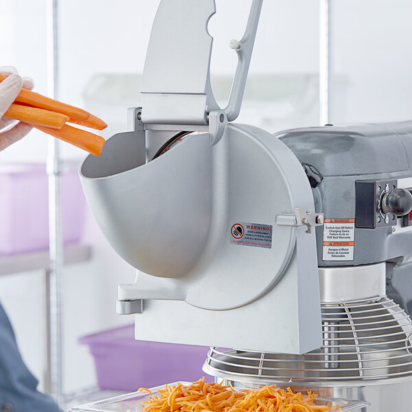 A person using a Shredder Attachment to shred carrots in a machine.