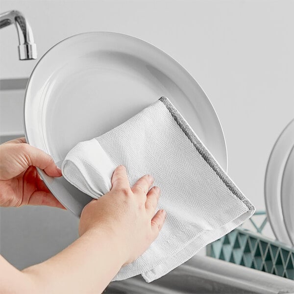 A person's hands drying a plate with a black-striped herringbone kitchen towel.