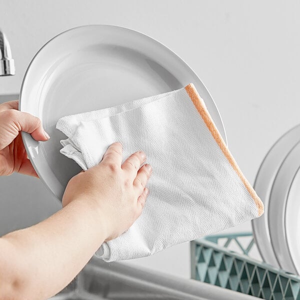 A person wiping a plate with a gold-striped herringbone kitchen towel.