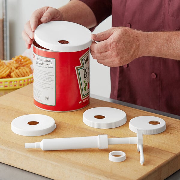 A white plastic condiment pump with tubes and round adapters on a wooden surface.