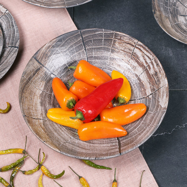 An Elite Global Solutions Denali melamine bowl with a knotwood embossed design filled with red and yellow peppers on a table.