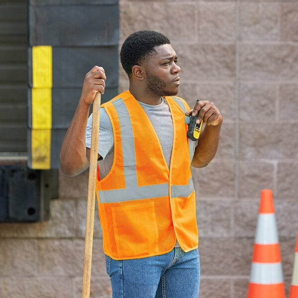 A man in an orange Ergodyne high visibility vest holding a tool.