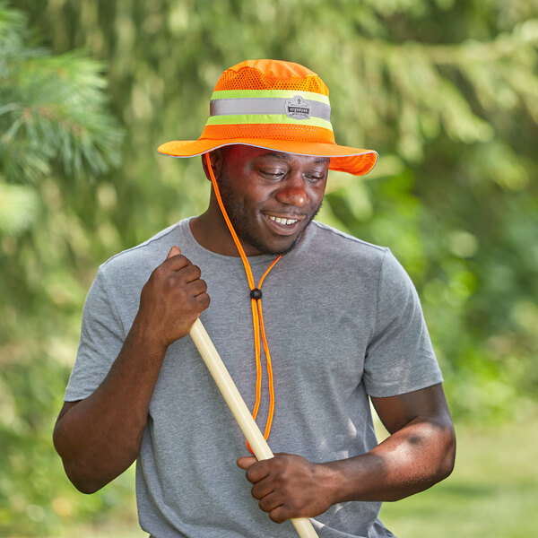 A man wearing an Ergodyne orange hi-vis ranger sun hat holding a stick.