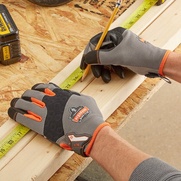A person wearing Ergodyne ProFlex heavy-duty work gloves measuring a piece of wood with a measuring tape.