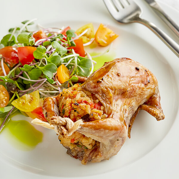 A plate of food with a whole quail, salad, and a fork and knife.