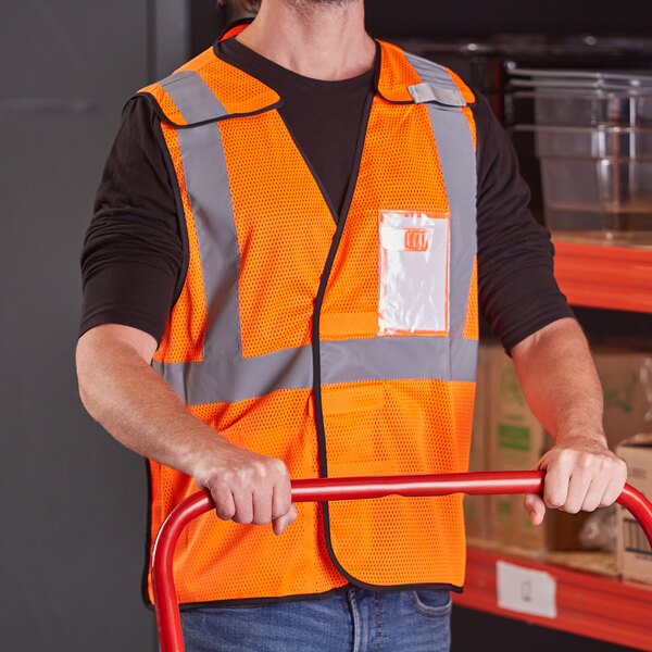 A man in an Ergodyne orange high visibility vest holding a red cart.