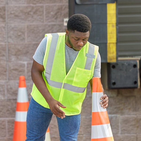 A man in a small/medium lime Ergodyne safety vest leaning on a traffic cone.