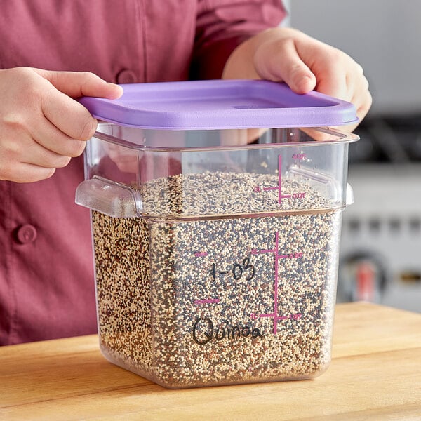 A woman holding a Vigor square clear food storage container filled with seeds with a purple lid.