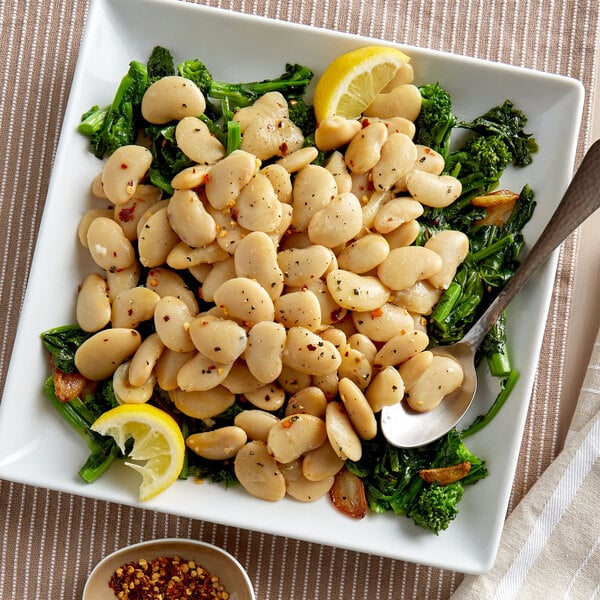 A plate of Furmano's butter beans with broccoli and a lemon wedge.
