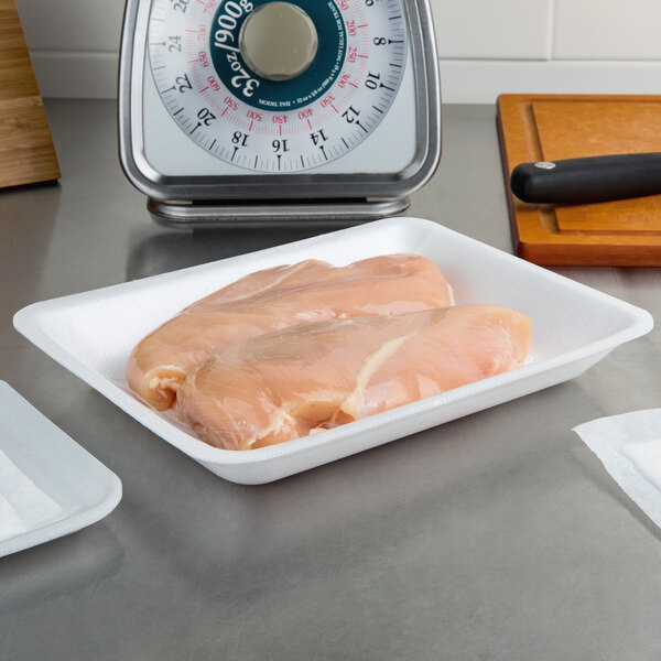 A white foam meat tray with raw chicken on a counter.