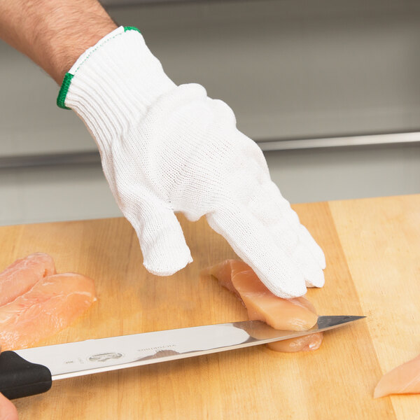 A person wearing a Victorinox cut resistant glove cutting meat on a cutting board.