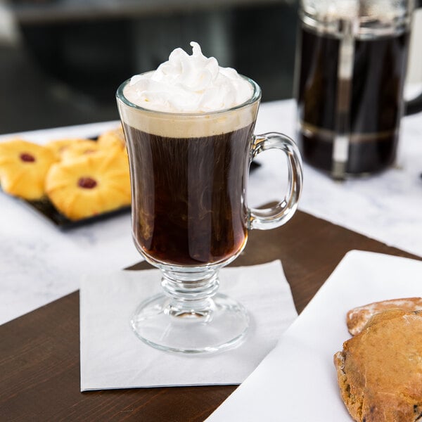 A Libbey Irish Glass coffee mug filled with coffee and whipped cream on a saucer with a pastry.