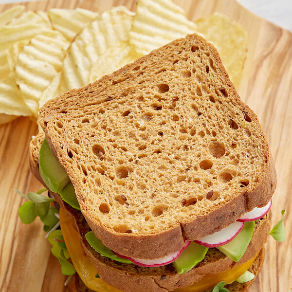 A sandwich with vegetables and a slice of Schar Gluten-Free Artisan Baker 10 Grains & Seeds Bread on a wooden board.
