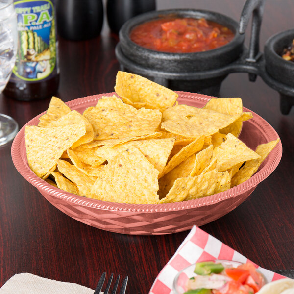 A round paprika polyethylene basket filled with chips and salsa on a table.