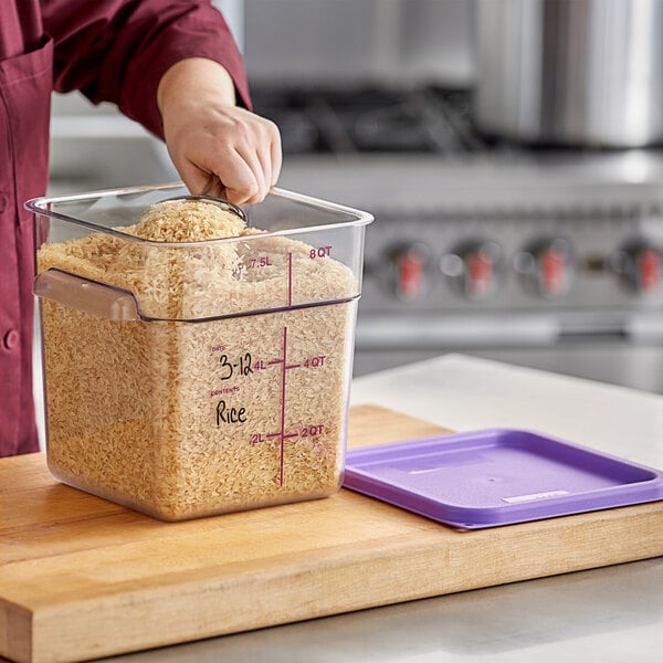 A person using a measuring cup to scoop rice into a purple Vigor food storage container.