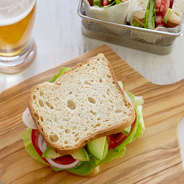 A sandwich made with Schar Gluten-Free Artisan Baker Sliced White Bread on a cutting board next to a glass of beer.