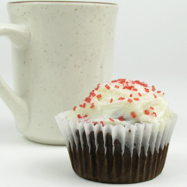 A cupcake with white frosting and red sprinkles in a white fluted paper wrapper.