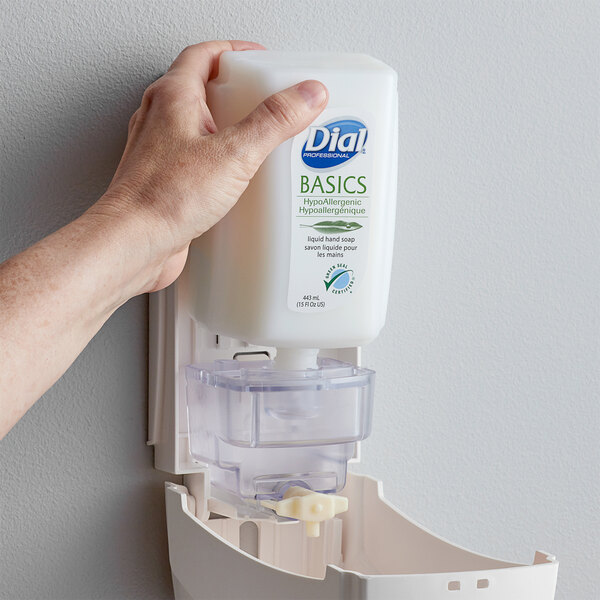 A hand holding a white bottle of Dial Basics liquid hand soap.