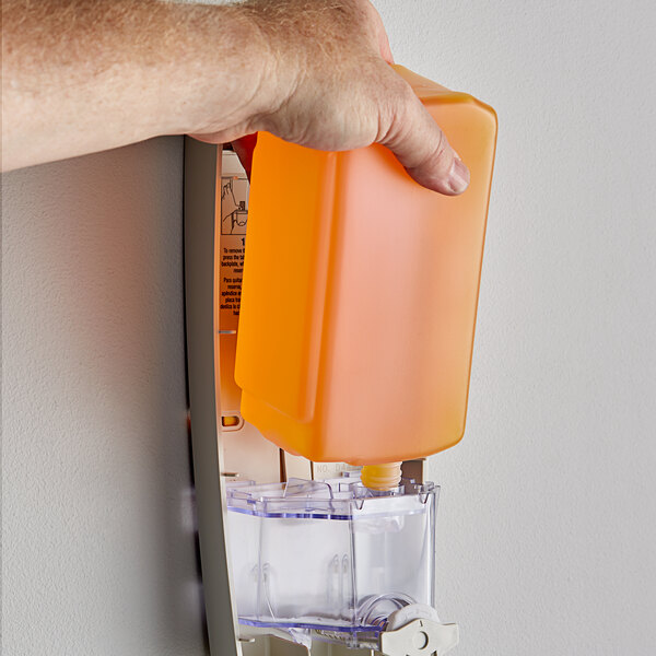 A hand holding a Dial gold liquid soap dispenser over an orange.