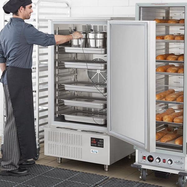 A man wearing an apron standing next to a large Avantco reach-in blast chiller.