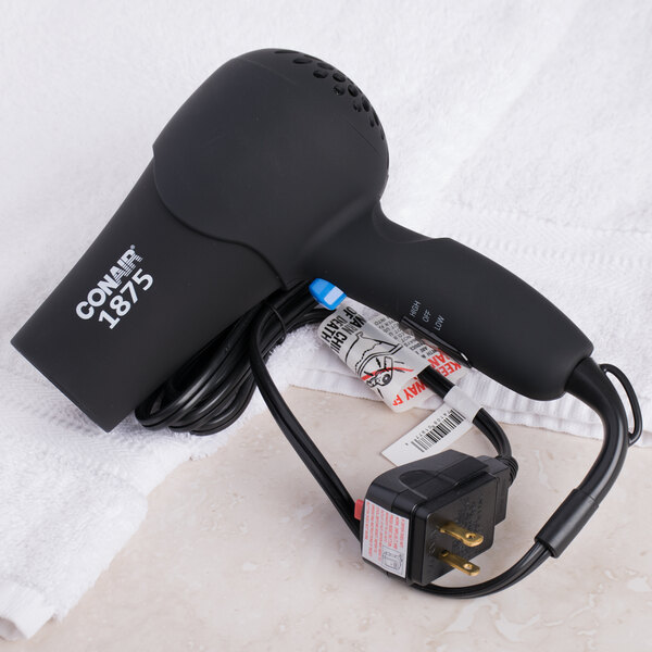 A Conair black hair dryer with a black cord sitting on a white towel.