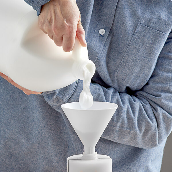 A person pouring coconut oil conditioner into a container using a white funnel.
