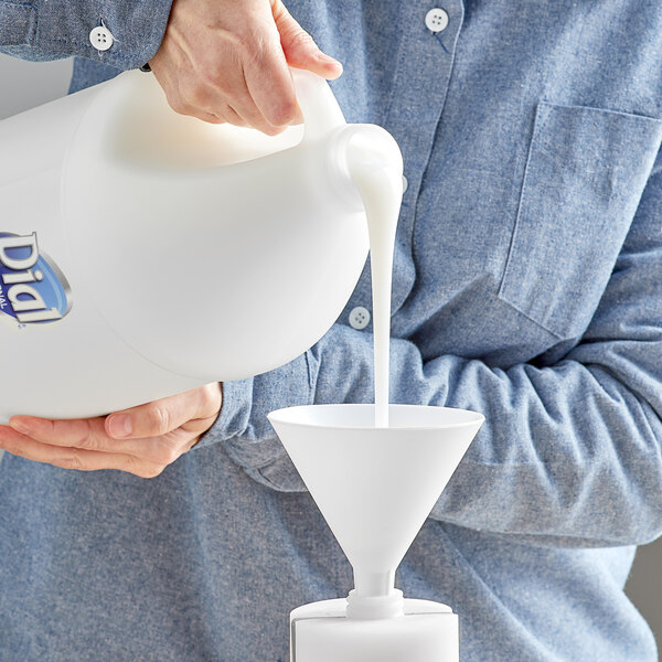 A person pouring liquid soap into a white container using a white funnel.