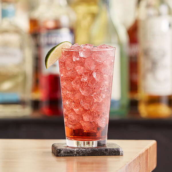 A Libbey mixing glass filled with ice and red liquid with a lime wedge on the rim.