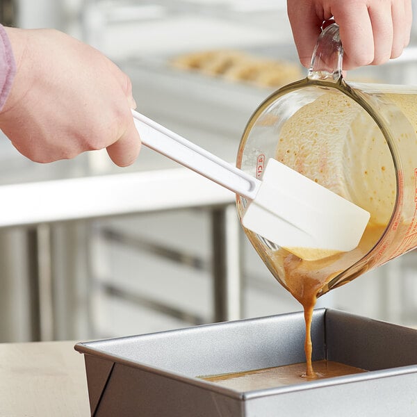 A hand using a Choice white spatula to pour brown liquid into a pan.