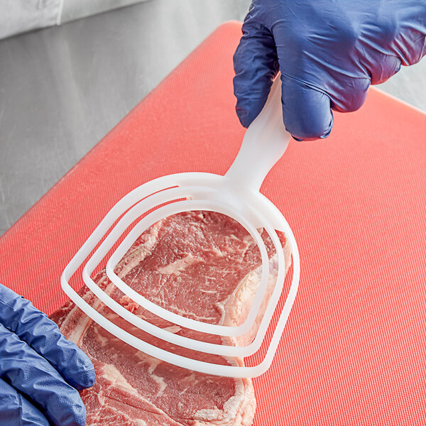 A person wearing a blue glove uses a Choice bone dust scraper to cut meat on a counter.