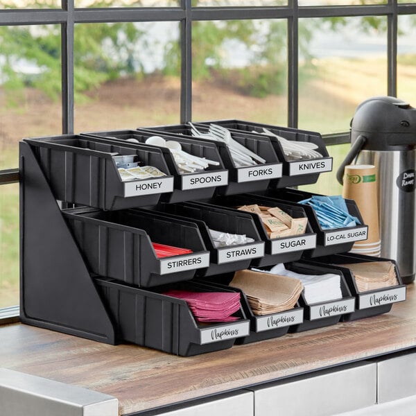 A black Choice 3-tier self-serve organizer with bins and labels on a counter.
