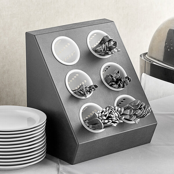 A white plastic flatware organizer with white perforated cylinders holding silverware.