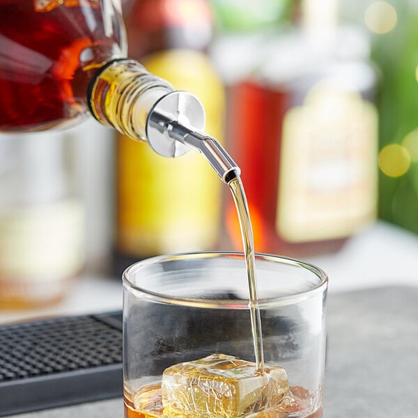 A person using a Choice Chrome whiskey pourer to pour whiskey into a glass with ice.
