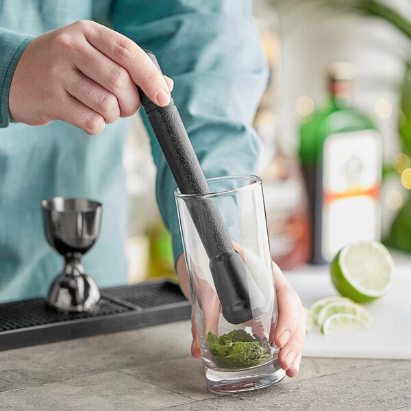 A person using a Choice black smooth head muddler to make a cocktail.