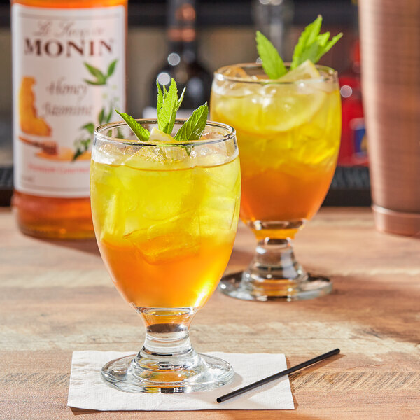 Two glasses of honey jasmine flavored drinks with ice and mint leaves.