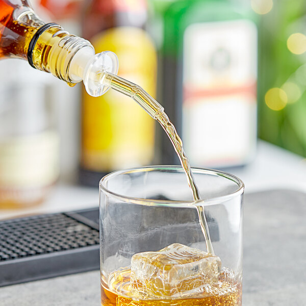A person using a Choice clear whiskey pourer to pour whiskey into a glass with ice.