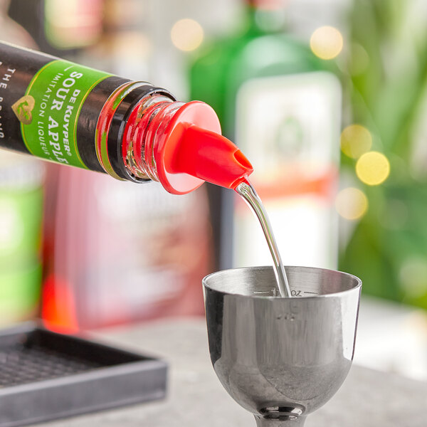 A close-up of a bottle of red liquid being poured through a neon red liquor pourer.