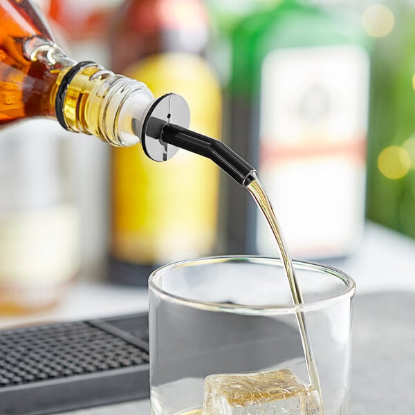 A person using a black Choice whiskey pourer to pour yellow liquid into a glass.