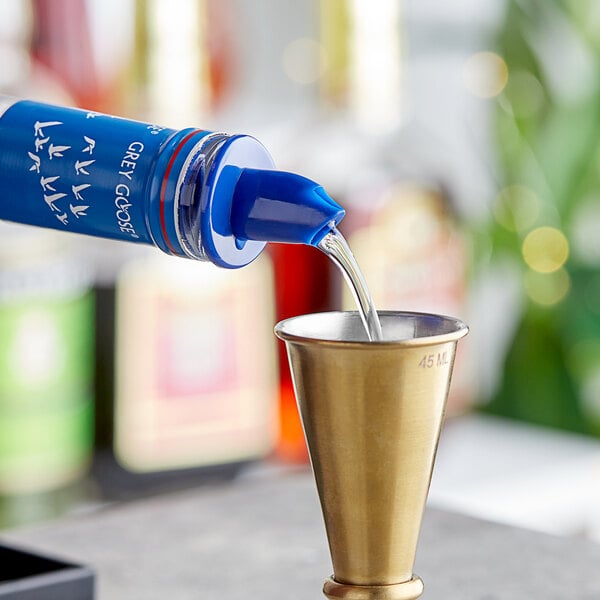 A blue bottle with a blue Choice Liquor Pourer pouring liquid into a gold cup.