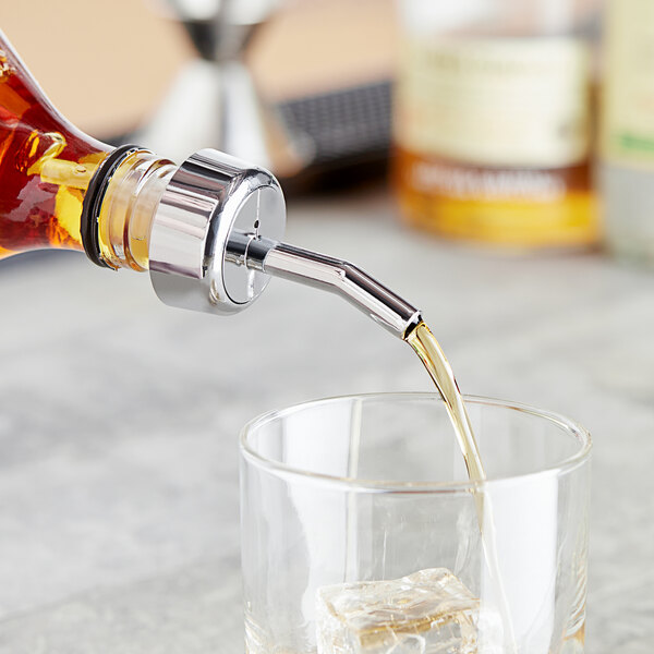 A bottle of whiskey with a Choice chrome whiskey pourer pouring whiskey into a glass.