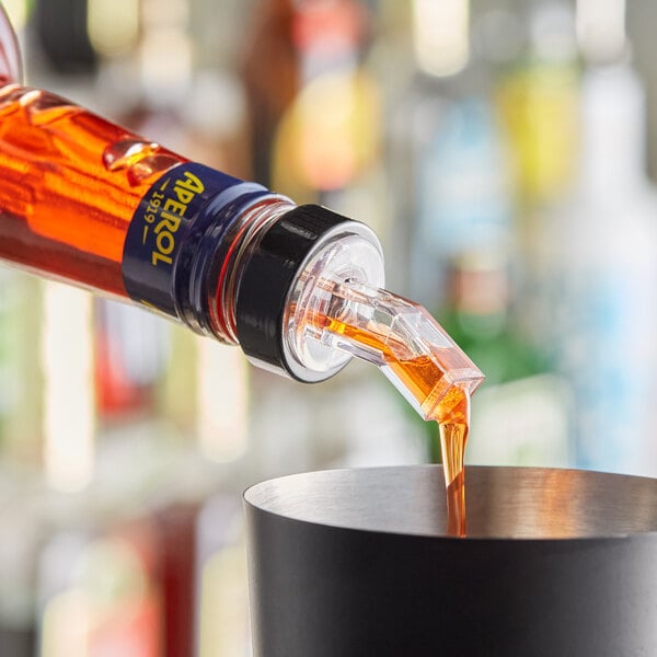 A person using a Choice clear liquor pourer to pour orange liquid into a cup.
