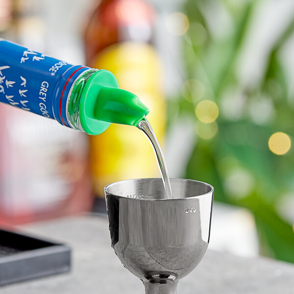 A person using a neon green Choice free flow liquor pourer to pour liquid into a cup.