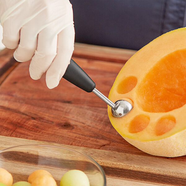 A person using an OXO melon baller to scoop melon balls out of a yellow melon.