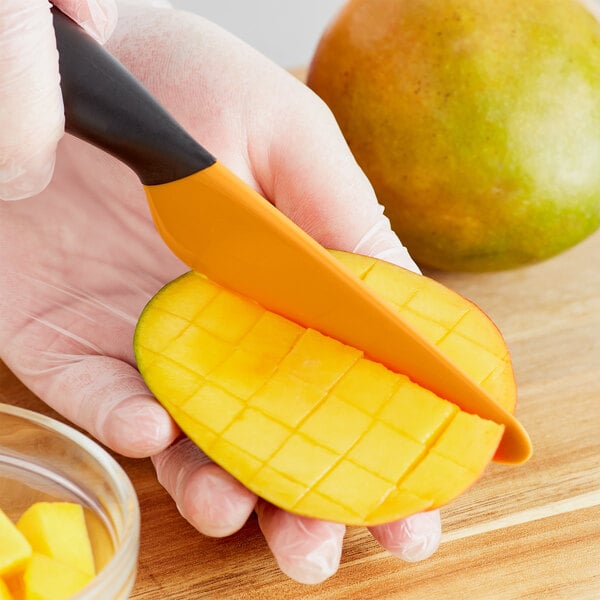 A person using an OXO mango slicer to cut a mango.