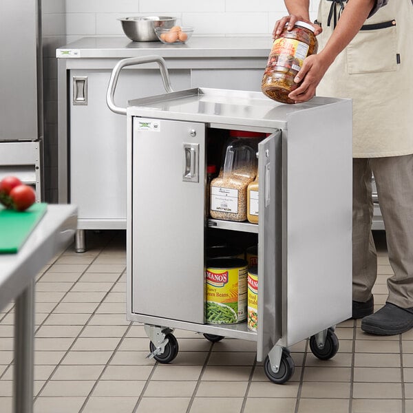 A man putting a jar of food into a Regency stainless steel utility cart with enclosed doors.